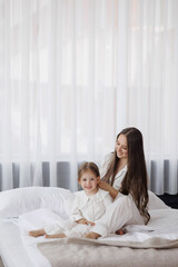 Mother and daughter enjoy relaxing time at home together in cozy white outfits