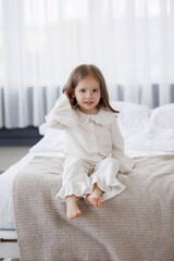 Fototapeta premium Young girl with long hair sits on bed in cozy bedroom during bright morning hours
