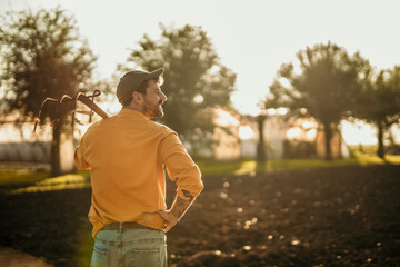 Farmer looking at his field at sunset holding a pitchfork