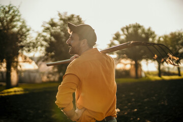 Farmer carrying pitchfork on shoulder in field at sunset