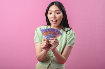 Asian woman looking surprised and excited while holding a fan of Indonesian rupiah banknotes,...