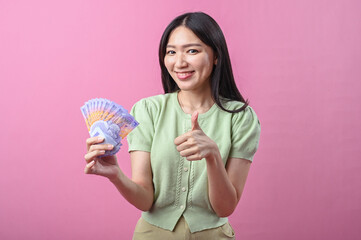 Asian woman in green top making OK hand gesture while holding Indonesian rupiah banknotes and...