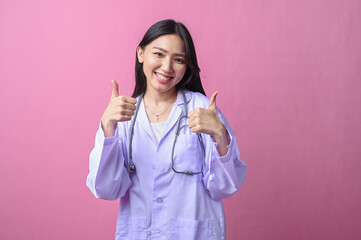 Asian female doctor smiling confidently while making an OK hand gesture, wearing a white medical...