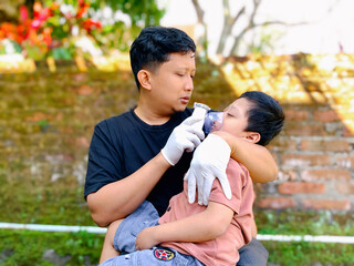 Father giving nebulizer therapy to his sick son outdoors