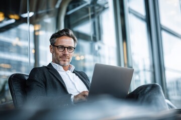 Fototapeta premium Mature professional man using laptop in modern office lounge, portraying remote work, business confidence, and digital productivity.