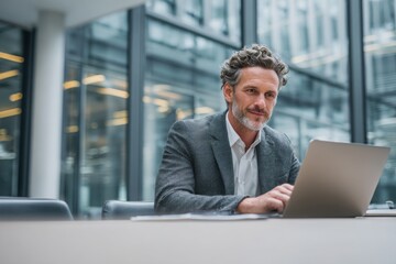 Mature professional man using laptop in modern office lounge, portraying remote work, business confidence, and digital productivity.
