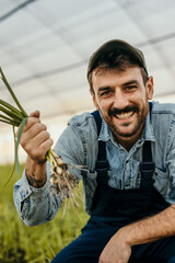 Farmer showing green onions in greenhouse, smiling at work
