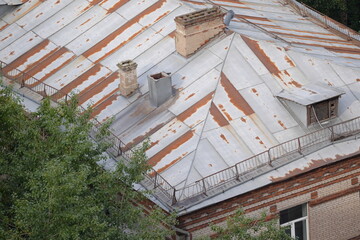 Old rusty metal roof of a historic brick building with chimneys and ventilation shafts

