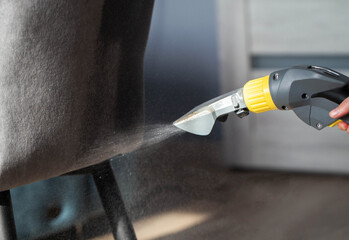 Spraying a chemical from a washing vacuum cleaner when cleaning the fabric upholstery of a chair....