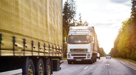 A column of trucks with semi-trailers transports cargo along a country road. Logistics company for...