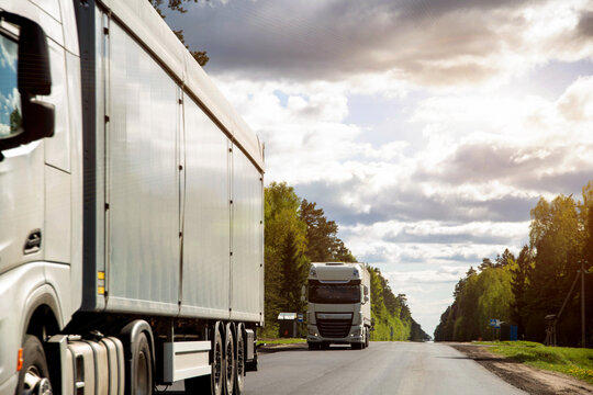 A column of trucks with semi-trailers transports cargo along a country road. Logistics company for the delivery of consolidated cargo. GPS tracking and cargo insurance.