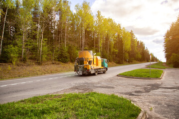 Old concrete mixer car driving along country road against forest background in summer, industry
