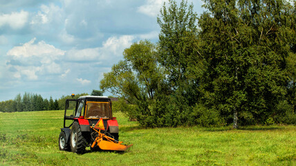 Roadside mowing of grass with a tractor near the road. Mowing roadsides, maintaining roadside areas, copy space for text. Road maintenance organization © HENADZY