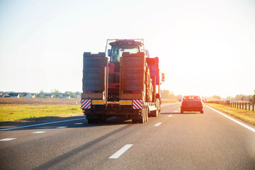 Transportation of a tractor by a truck with a lowboy semitrailer on a highway against the backdrop...