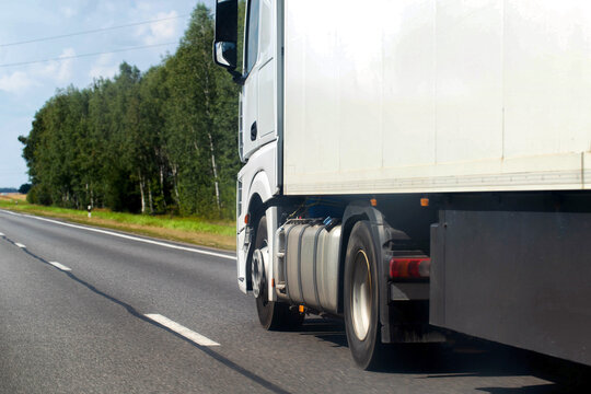 A truck with a semi-trailer drives along a highway against the backdrop of a forest in summer. Concept of won cargo tenders, carrier rating. Copy space for text
