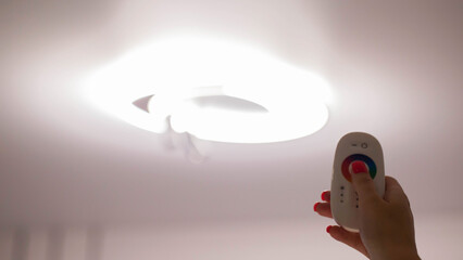 Remote control in hand against the background of a ceiling diode chandelier. Concept of remote...
