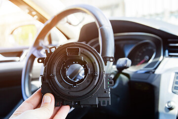 A man holds a steering column cable of a car in his hand against the background of a steering wheel, electrical failure