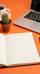 Open notebook with lined pages, laptop, coffee cup, and cactus on orange background, showcasing workspace mockup, ideal for productivity or business concepts
