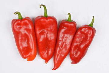 Four vibrant red peppers with green stems are arranged horizontally on a plain white background, ready for culinary use.