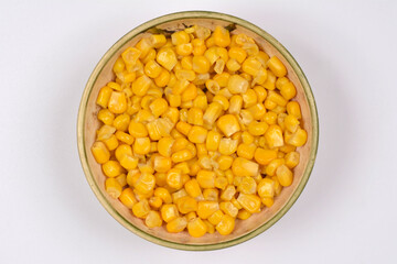 An overhead shot showcases a rustic ceramic bowl brimming with bright, yellow corn kernels, presented against a clean white background