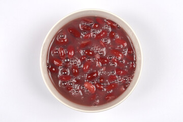 An overhead shot displays a white bowl filled with glistening red kidney beans in their liquid, centered on a plain white background