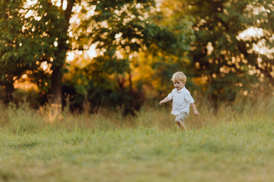 Cute little boy with blond hair running in the park at sunset, healthy outdoor games, walk in summer and spring, active family leisure. insects and mosquitoes in the air biting children.