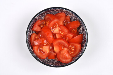 An overhead shot captures a blue and white patterned bowl filled with freshly sliced red tomatoes, centered on a plain white background
