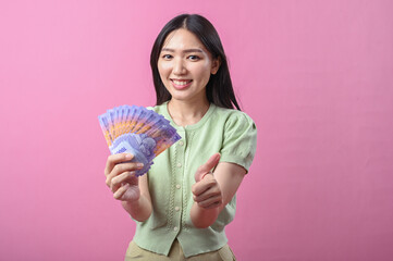 Asian woman in green top making OK hand gesture while holding Indonesian rupiah banknotes and...
