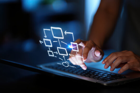 Person typing on laptop with flowchart overlay on screen in a dark room with blue light glow