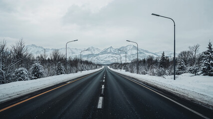 Empty asphalt road leading to snowy mountains in winter