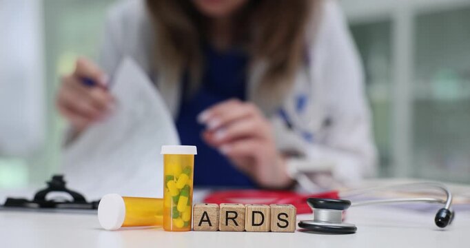 Wooden cubes spell ARDS put on lab table creating emergency topic. Female medic studies patient paper fighting lung failure risk near pill containers