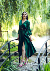 Elegant young woman in a green dress walking confidently on a small arched bridge surrounded by...