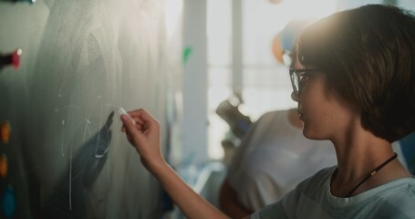 Smart Pupil Showcasing Math Knowledge: Close Up Shot of Elementary School Boy Solving Mathematical Problems Writing on the Chalkboard in Front of Classroom. Female Teacher Checking Correct Answers.