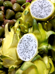  A vibrant display of yellow dragon fruit (pitahaya), with one fruit cut open to reveal its striking white flesh speckled with tiny black seeds, surrounded by other whole fruits.