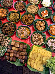 A vibrant, close-up view of a street food stall displaying numerous platters of various traditional Indonesian dishes ready to be chosen by customers.