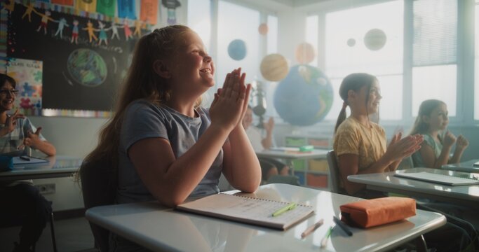 Cheerful Diverse Kids Sitting at Desks, Clapping Their Hands, Interacting with Teacher During Dynamic Gamified Activity. Female Teacher Providing Interactive Lesson to Elementary School Students.