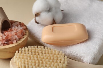 Soap bar, brush, sea salt, towel and cotton flower on beige background, closeup