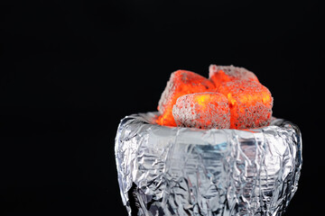 Smoldering charcoal cubes on hookah holder covered with foil against dark background, closeup....
