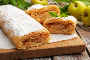 Tasty apple strudels with powdered sugar, mint and fruits on wooden table, closeup