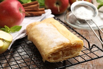 Tasty apple strudel with powdered sugar, mint, fruits and cinnamon on wooden table, closeup