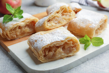 Pieces of tasty apple strudel with powdered sugar and mint on light grey table, closeup