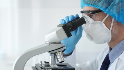 Male scientist wearing protective gear examining microscope slide, analyzing research sample in sterile laboratory environment. Health care and science concept