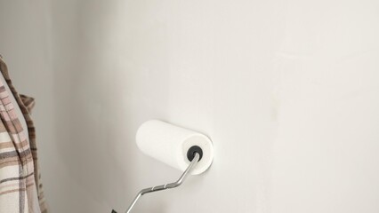 Painter's gloved hand gripping paint roller, spreading white paint across wall during home interior...