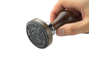 Close up shot of a hand holding a wooden handled rubber stamp with intricate design details visible on it