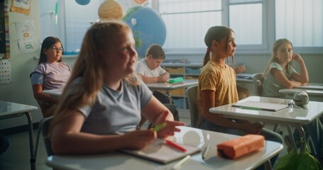 Primary School Children Sitting at the Desks, Listening to Lecture from Teacher, Raising Hands to Give Correct Answer. Group of Young Boys and Girls Learning Geography or Science in Modern Classroom.