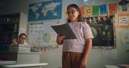 Primary School Girl Holding Notebook Speaking, Showcasing Knowledge of Geography in Front of...