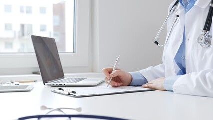 Doctor woman completing healthcare paperwork, clipboard positioned near laptop and stethoscope in...