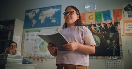 Primary School Girl Holding Notebook Speaking, Showcasing Knowledge of Geography in Front of...
