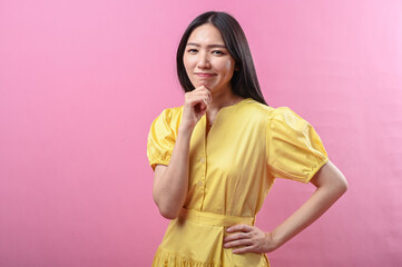 Asian woman in a yellow dress smiling gently with her hand resting under her chin, posing...