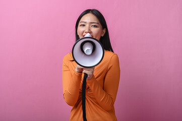 Asian woman with long black hair wearing an orange dress holding a megaphone directly facing the...